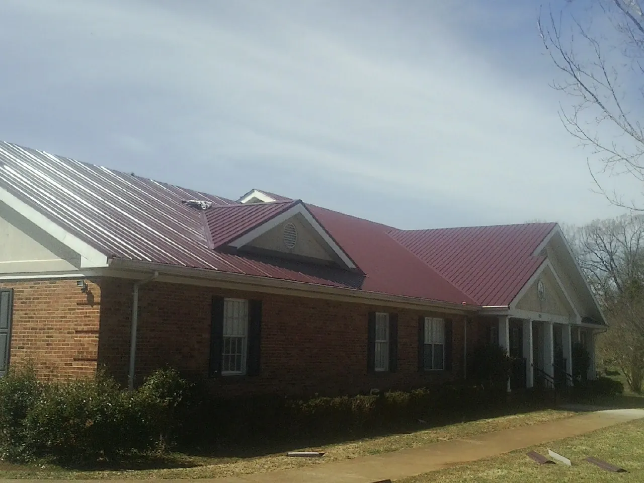 Red metal roof with gabled entries on a long brick building, from a Hail Damage Roof Repair job in Moorhead