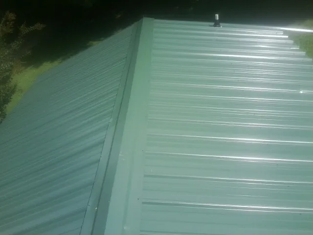 New green metal panels meeting at the ridge of a roof — Flat Roof Repair work by our crew in Moorhead
