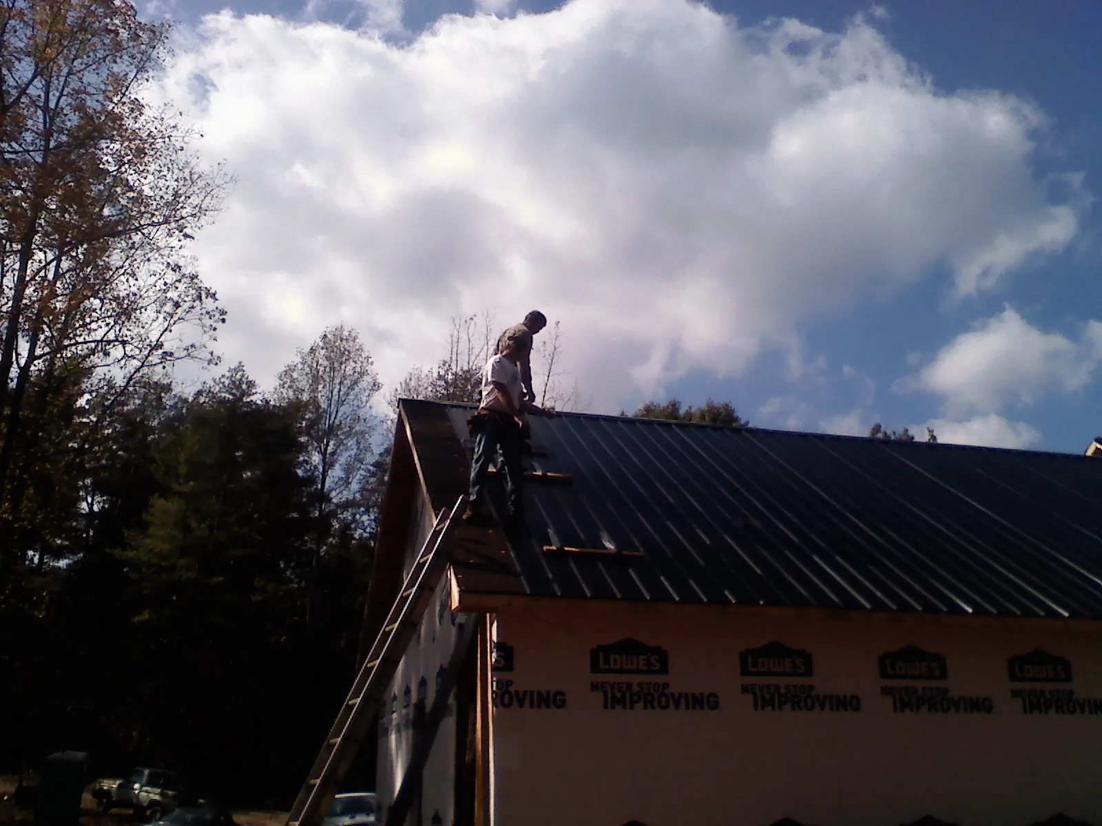 Roofer fastening dark metal panels high against a cloudy sky, from a Roof Inspection job in Moorhead