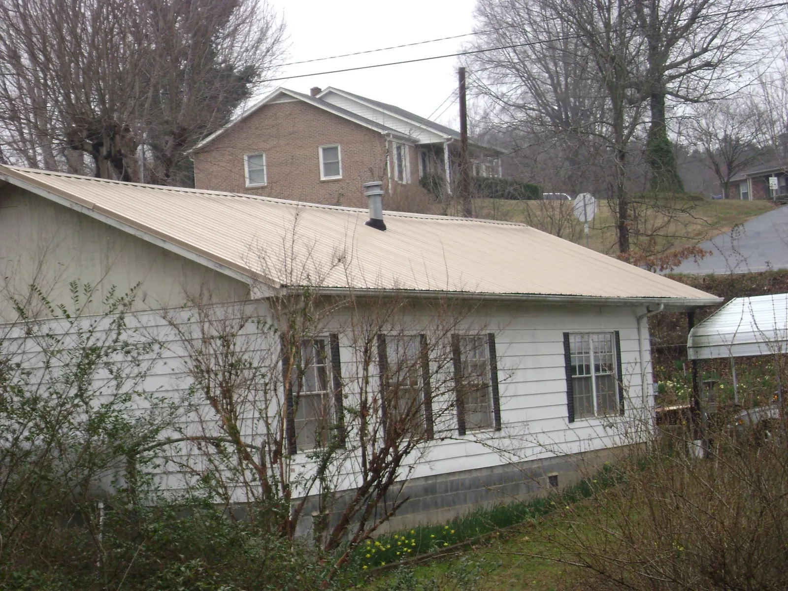Tan metal roof on a white sided house set into a hillside — Commercial Roofing by Roofing Brothers in Moorhead